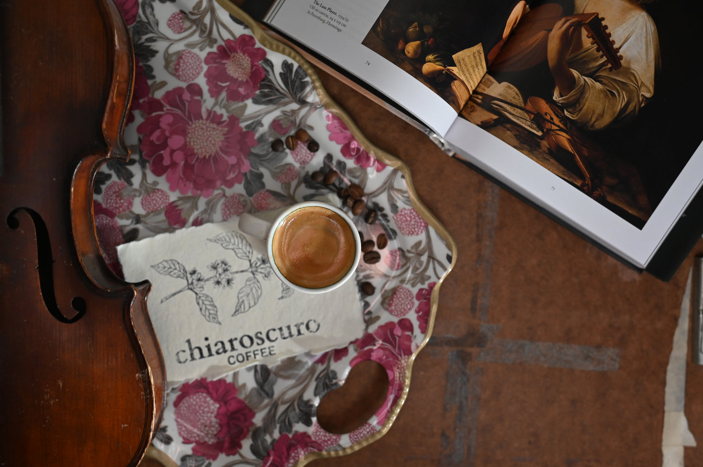 Espresso in a white mug on a floral tray with coffee beans and a book, featuring Chiaroscuro Coffee.