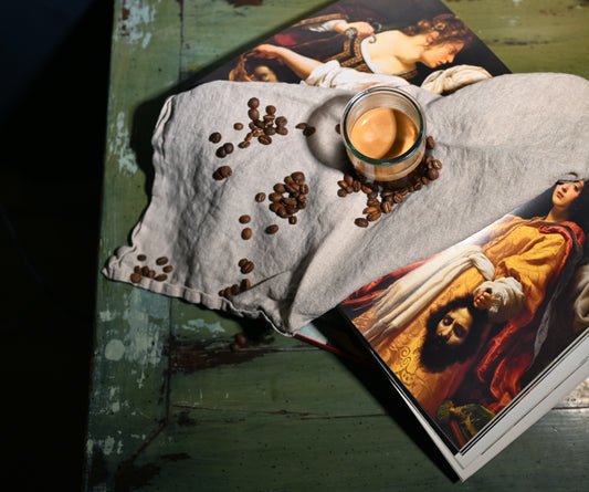 A glass of espresso on a linen cloth with coffee beans, set on colorful art books.