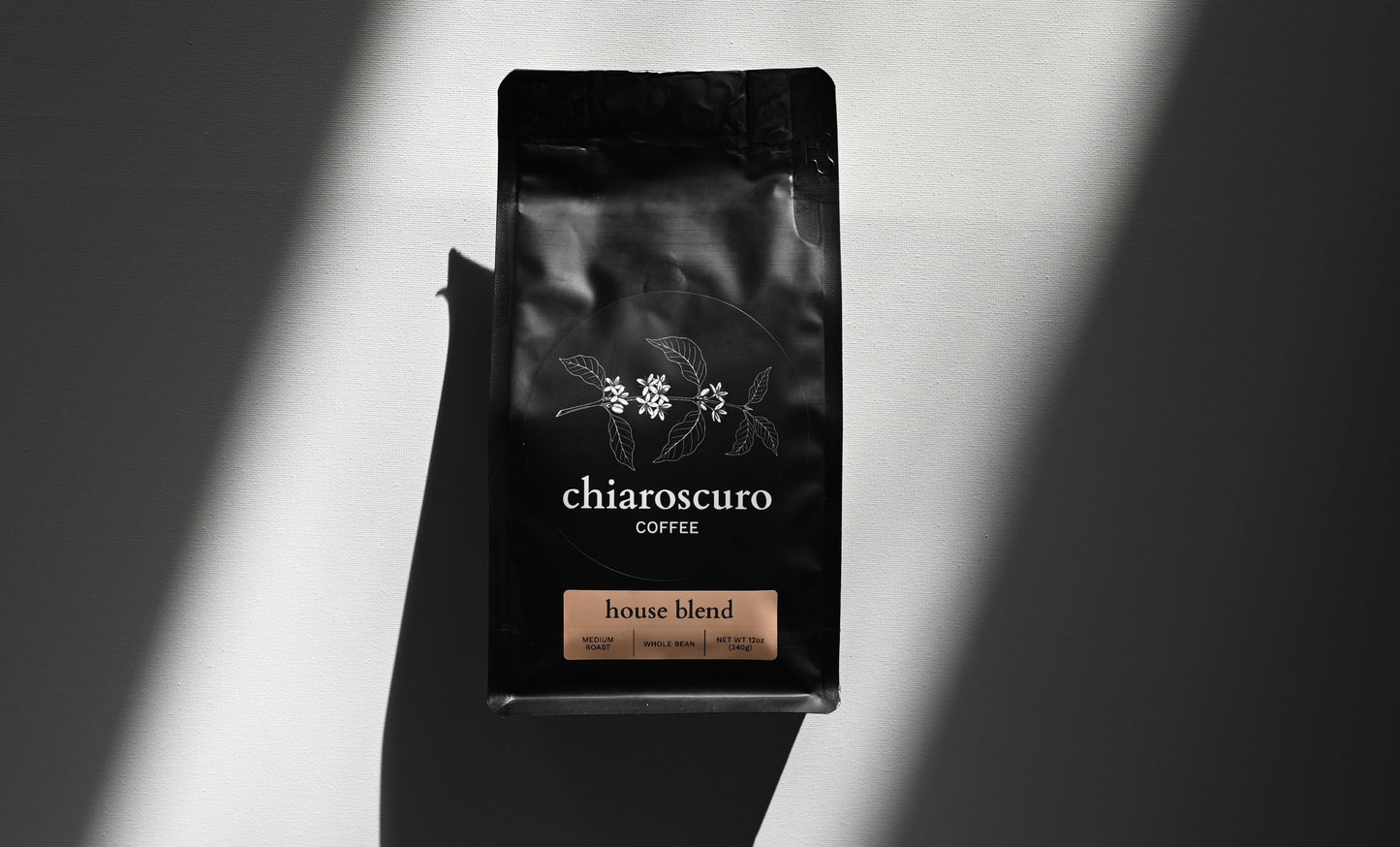 Chiaroscuro coffee house blend, medium roast, whole bean, 12 oz black packaging on a light background.
